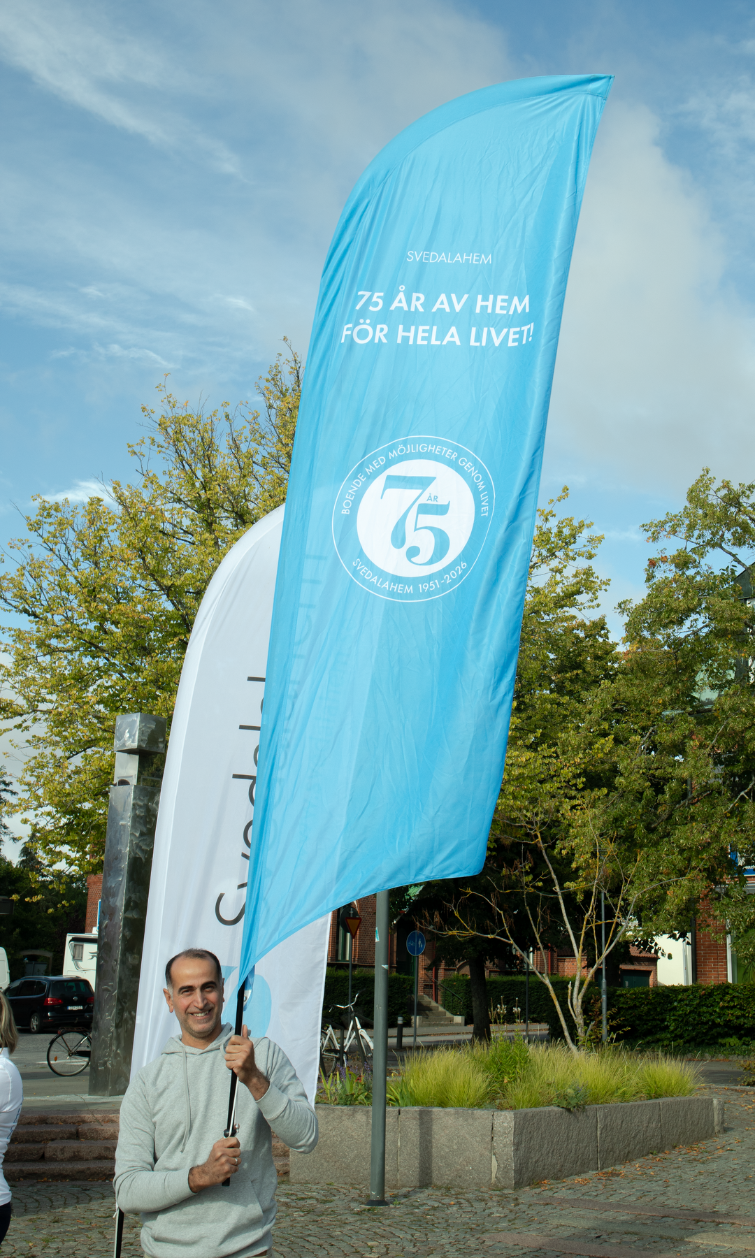 man om h&aring;ller en bl&aring; beachflagga med Svedalahem 75 &aring;r